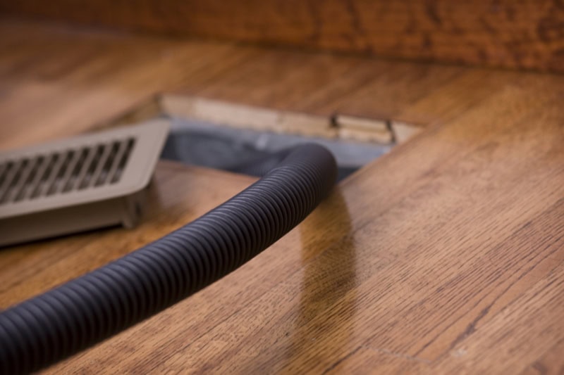 Breathe Easy This Holiday Season: Why Duct Cleaning Matters. Photo of a hose running into an air duct vent for cleaning.